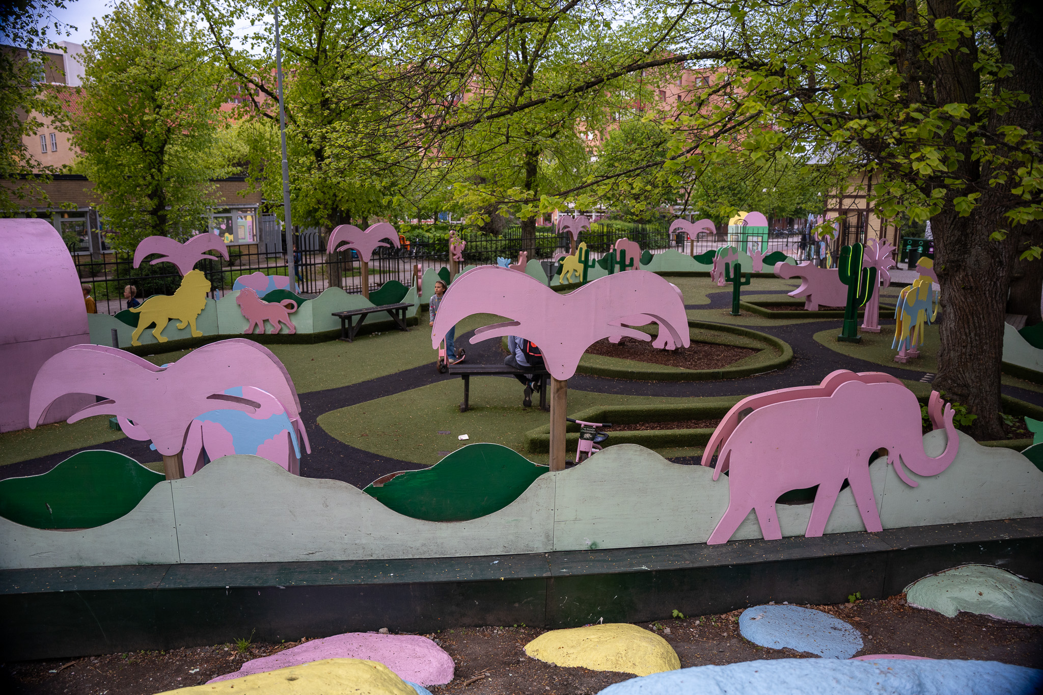 Bunter Spielplatz mit übergroßen rosa Elefanten- und Flamingofiguren zwischen grünen Hügeln