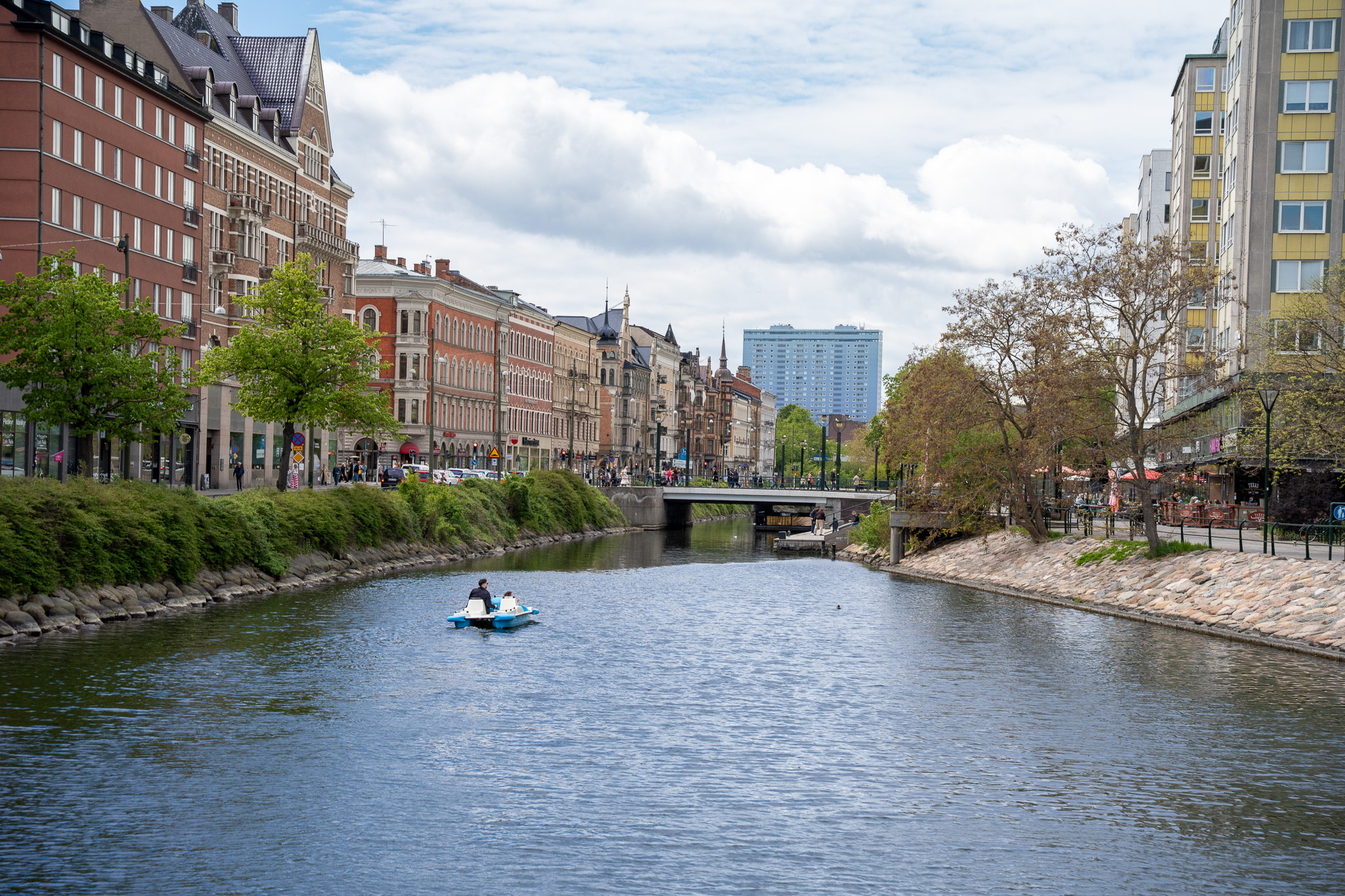 Stadtkanal in Malmö mit einem Tretboot, am Ufer Backsteinhäuser und blühende Bäume