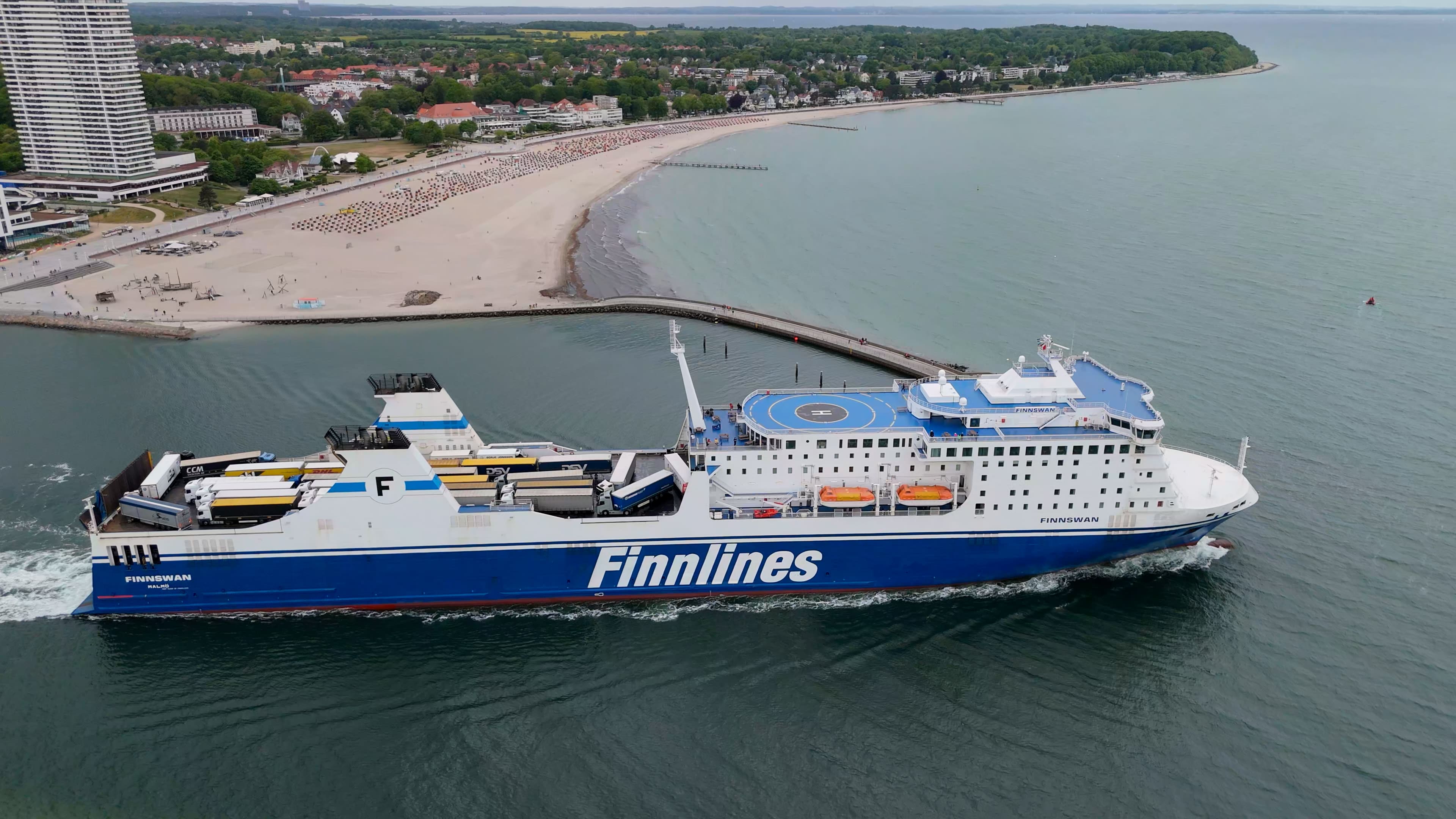 Luftbild der Finnlines-Fähre beim Einlaufen in Travemünde, links der Strand mit Strandkörben und das Maritim-Hochhaus