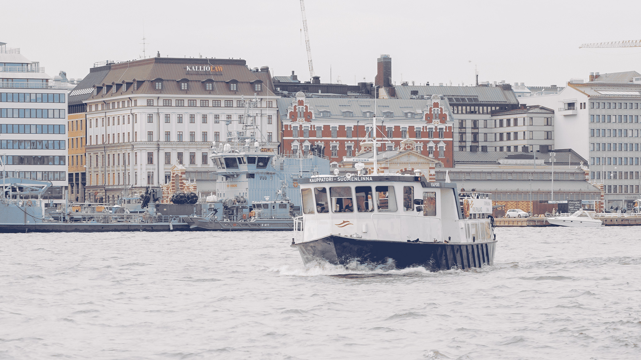 Kleine Hafenfähre auf dem Wasser vor der Uferzeile von Helsinki mit hellen Altbaufassaden