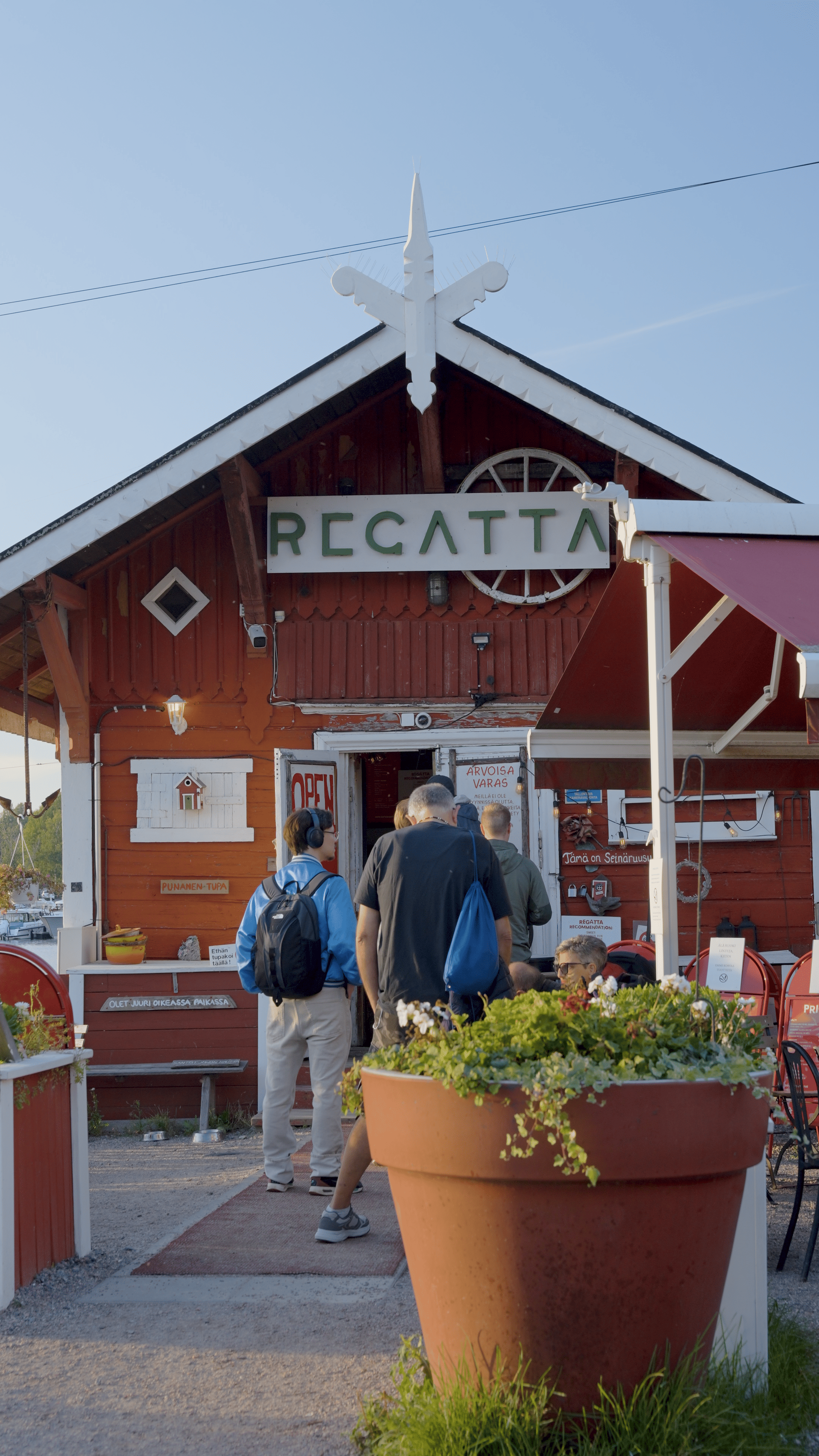 Rot gestrichenes Holzhaus des Café Regatta mit Gästen am Eingang und großen Blumenkübeln davor