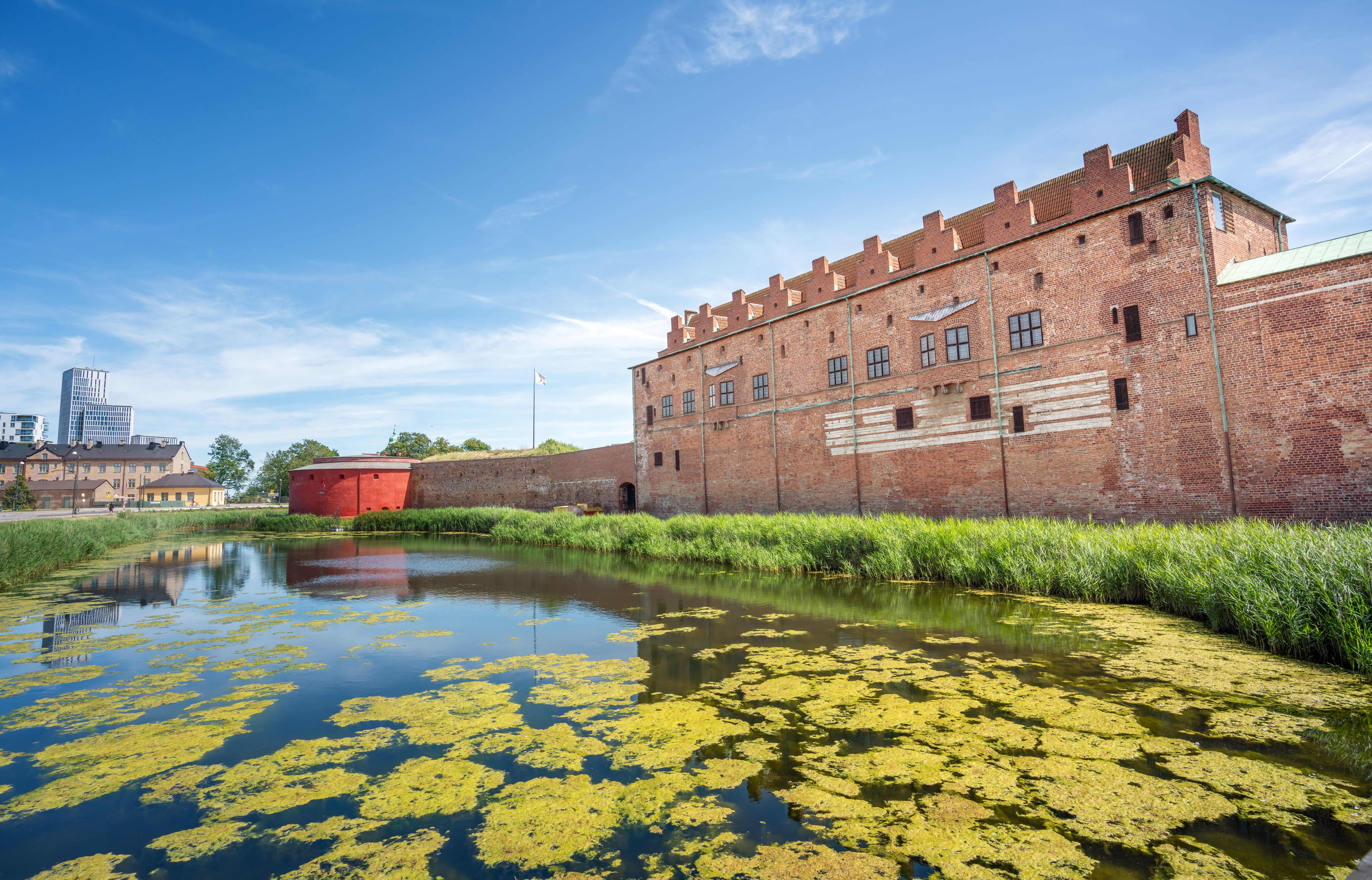 Schloss Malmöhus, ein niedriger Backsteinbau, hinter dem von Wasserlinsen bedeckten Burggraben