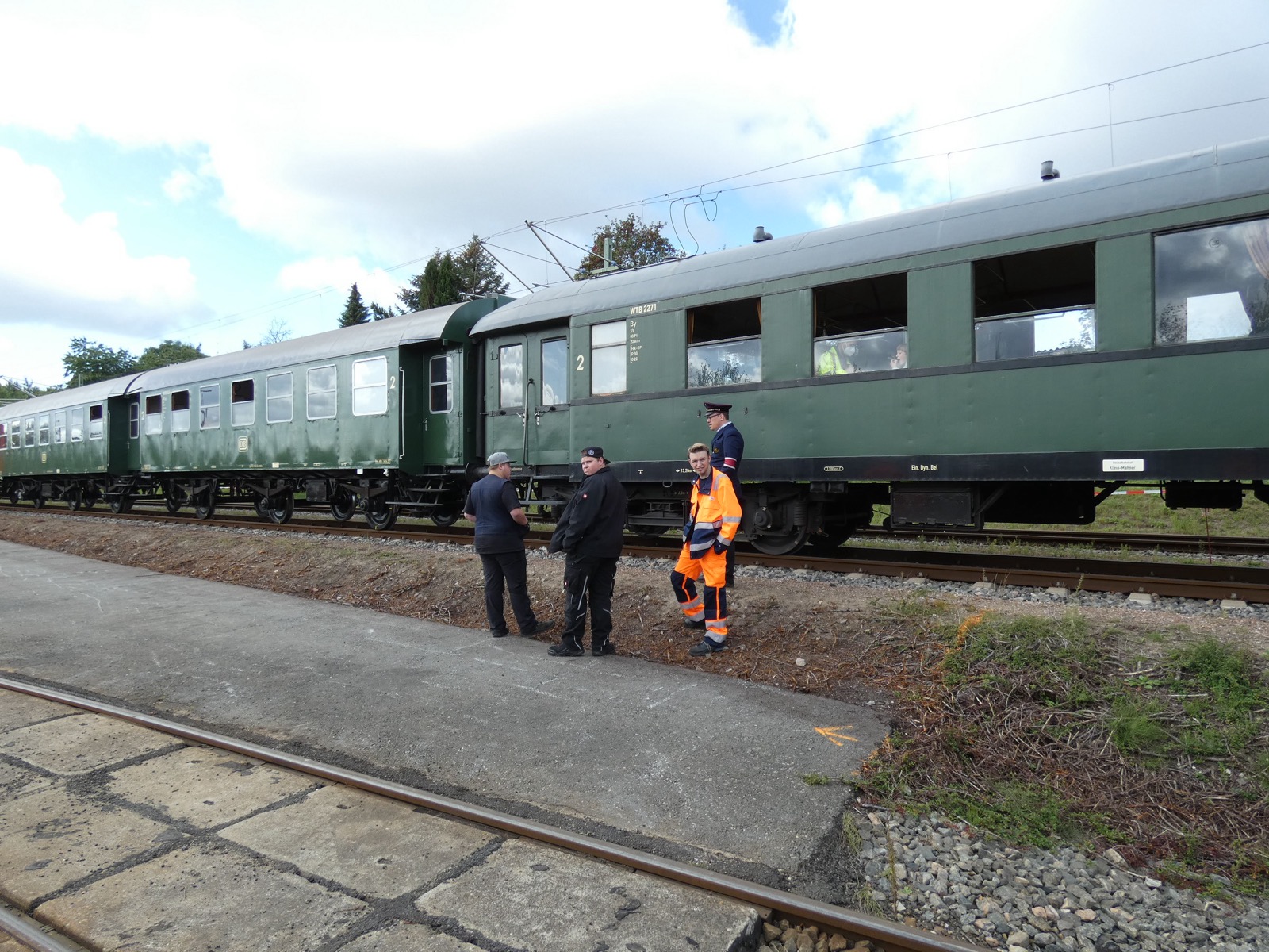 Grüne historische Reisezugwagen mit Zugpersonal am Bahnsteig