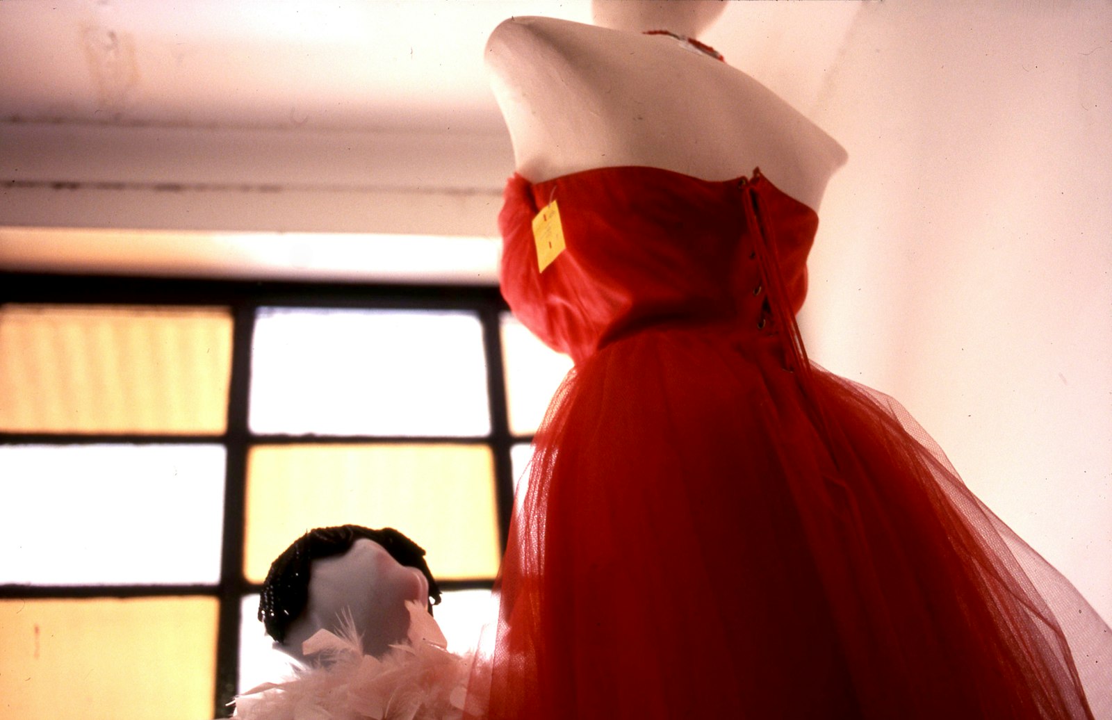 Schaufensterpuppe mit rotem Kleid neben einem Fenster